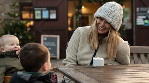 A mum and her two young children sit outside at the Timber Yard, enjoying a hot chocolate with whipped cream.